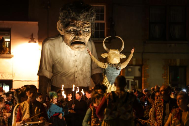 A photograph of a macnas parade at night. A large puppet is surrounded by people in costume and drummers