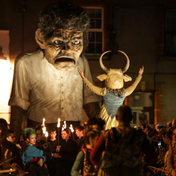 A photograph of a macnas parade at night. A large puppet is surrounded by people in costume and drummers