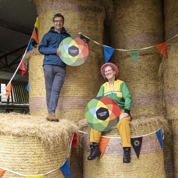 a man and woman sitting on hay bales holding colourful Culture Night signs
