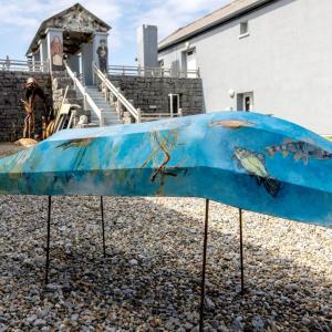 A photography outside of Áras Éanna Arts Centre. A currach stands in the foreground with sealife painted on it